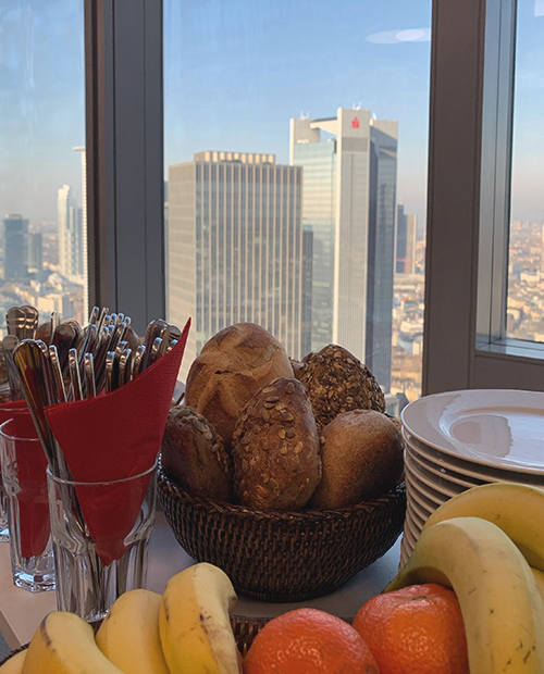 Banenen, Mandarinen, Brötchen auf einem Tisch im K-1 BusinessClub Main Tower, im Hintergrund Hochhäuser